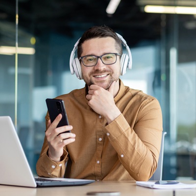 young man sitting at the desk wearing headphones, working on a laptop